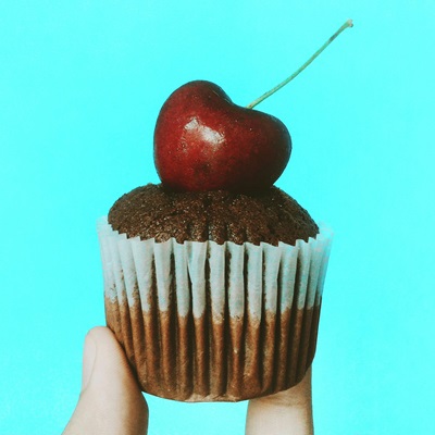 A cherry on top of a chocolate cupcake.