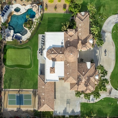 Aerial view of a large luxury estate with a pool, spa, putting green, and tennis court, surrounded by landscaped greenery and palm trees.