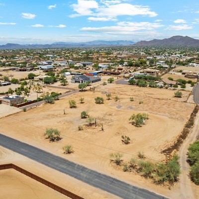 Aerial view of a residential neighborhood in a desert area, with scattered homes, dry terrain, and distant mountains.