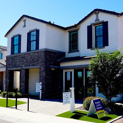 Two-story house with stone accents, blue shutters, and a small yard with signs. Sunny day.