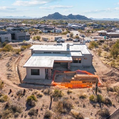 A luxury home under construction in a scenic desert community, surrounded by natural landscape and mountain views in the distance.
