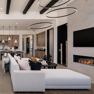 Spacious modern living area with high ceilings, exposed beams, a sleek kitchen island with pendant lighting, and a cozy seating area near a contemporary fireplace.