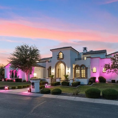 Luxury home exterior at sunset with vibrant pink smart lighting illuminating the landscape and architectural features, showcasing modern smart home technology.