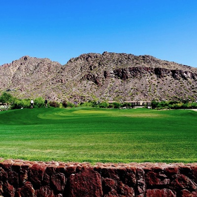 A beautiful green golf course with a blue sky and mountain in the background.