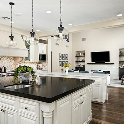 Luxury kitchen with white cabinetry, a large black island, and open view into the family room.