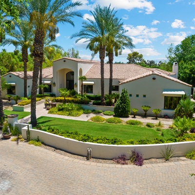 A luxurious home exterior with a circular driveway, vibrant landscaping, and tall palm trees surrounding the Mediterranean-style property.