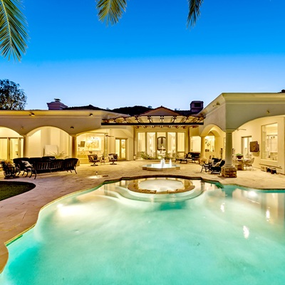 Stunning pool area of an Arizona mansion located in Paradise Valley with palm trees, outdoor seating, and a beautifully lit luxury home at twilight.