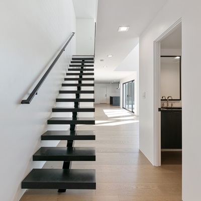 Open staircase with black floating steps and railing in a bright, minimalist townhome interior.