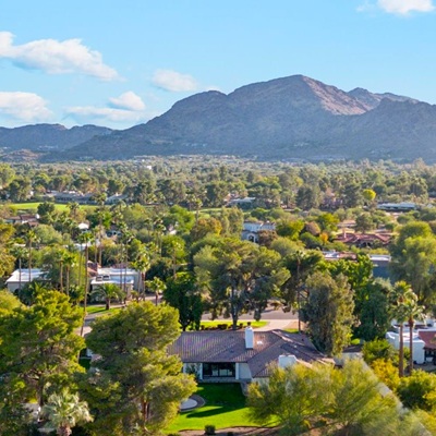 A scenic view of a Arizona neighborhood with palm trees and mountains in the background under a bright blue sky.