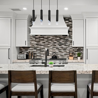 Contemporary kitchen with white cabinets, marble island, mosaic backsplash, and stainless steel appliances.