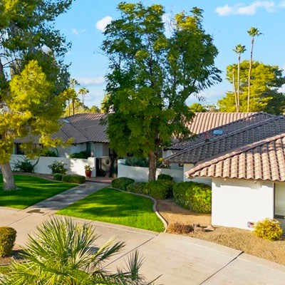 A front-facing ground view of the same elegant home, showcasing the manicured front lawn, mature trees, and a welcoming pathway leading to the entrance with tiled rooflines.