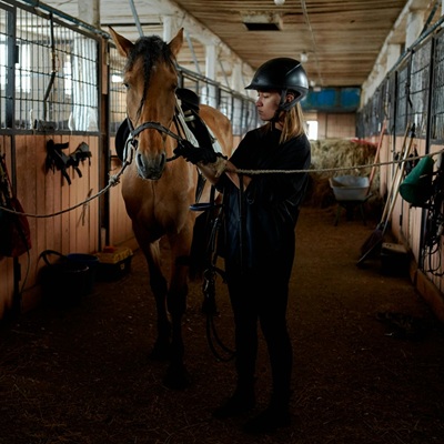A woman preparing a horse with reins in a stable.