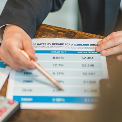 Hand pointing to a table of mortgage rates and monthly payments on printed documents.