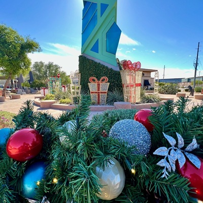 Holiday decorations near the Scottsdale Spire, featuring colorful ornaments, wrapped gift displays, and greenery under a bright sky.