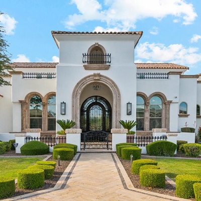 The front of an Arizona luxury home on a bright sunny day with scattered white puffy clouds.