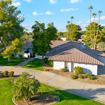 A beautiful single-story home with a tiled roof, surrounded by well-manicured lawns, trees, and a curved driveway on a sunny day.