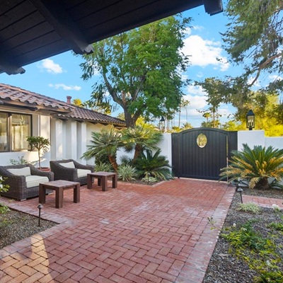 Courtyard with seating area, brick flooring, lush greenery, and a gated entrance.