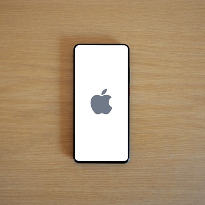 A smartphone with the Apple logo on its screen rests on a wooden surface.