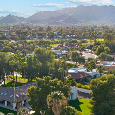 A scenic aerial view of a lush neighborhood with palm trees, homes, and mountains in the background.