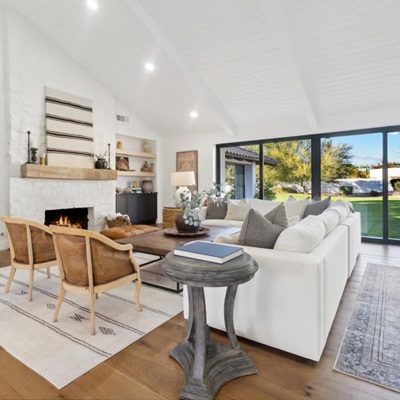 A bright and spacious living room with a vaulted white ceiling, a cozy fireplace, built-in shelves, and large sliding glass doors that open to a lush backyard.