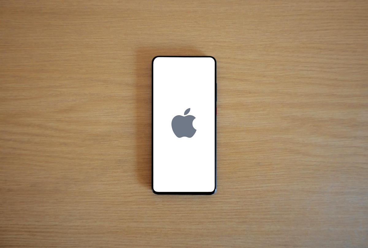 A smartphone with the Apple logo on its screen rests on a wooden surface.