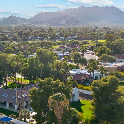Aerial view of a lush Greater Phoenix suburb with palm trees, single-story homes, and mountains in the background.