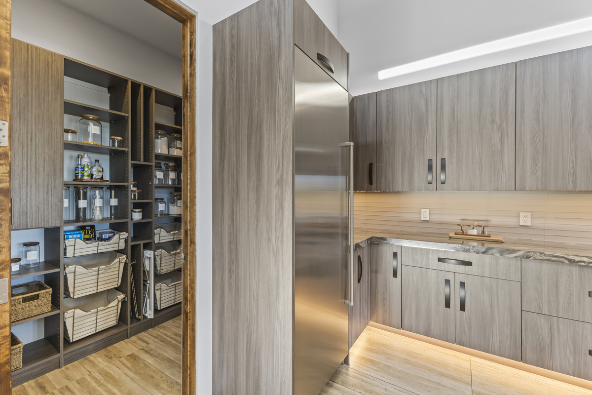 Modern kitchen and organized pantry with sleek gray cabinetry and stainless steel appliances.