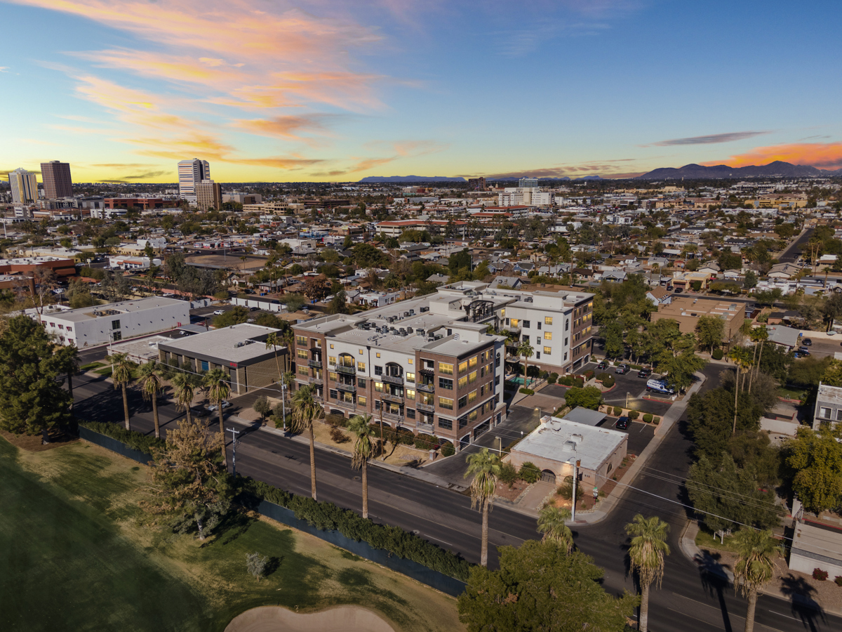 Urban Greater 
Phoenix aerial view with modern buildings, homes, and a distant skyline under a sunset.
