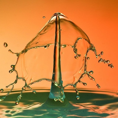 A high-speed close-up of a water splash forming a symmetrical, umbrella-like shape against an orange background.