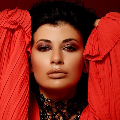 A dark-haired fashion model wearing red and looking into the camera.