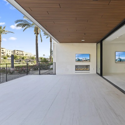 Expansive covered patio opening to the living room via pocket glass doors, showcasing a sleek fireplace, light plank flooring, and palm‑lined resort views.