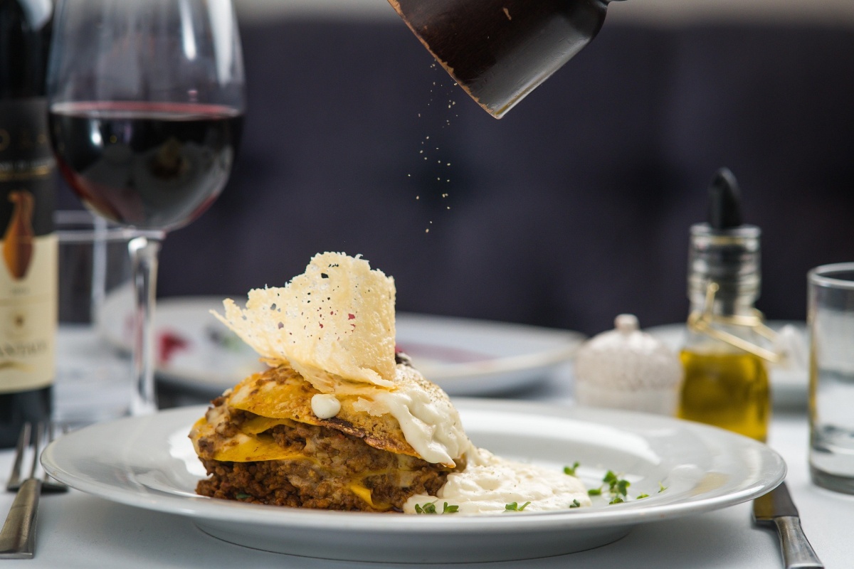 Clean presentation of a lasagna dish on a plate being sprinkled with pepper