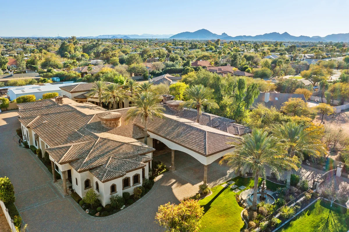 Aerial view of estate with tile roof, palm trees, and mountain backdrop.