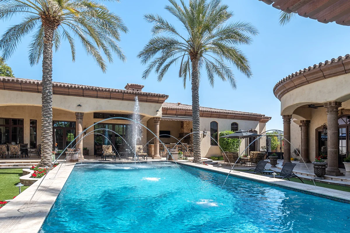 Luxury backyard with pool fountains, palm trees, and patio seating.