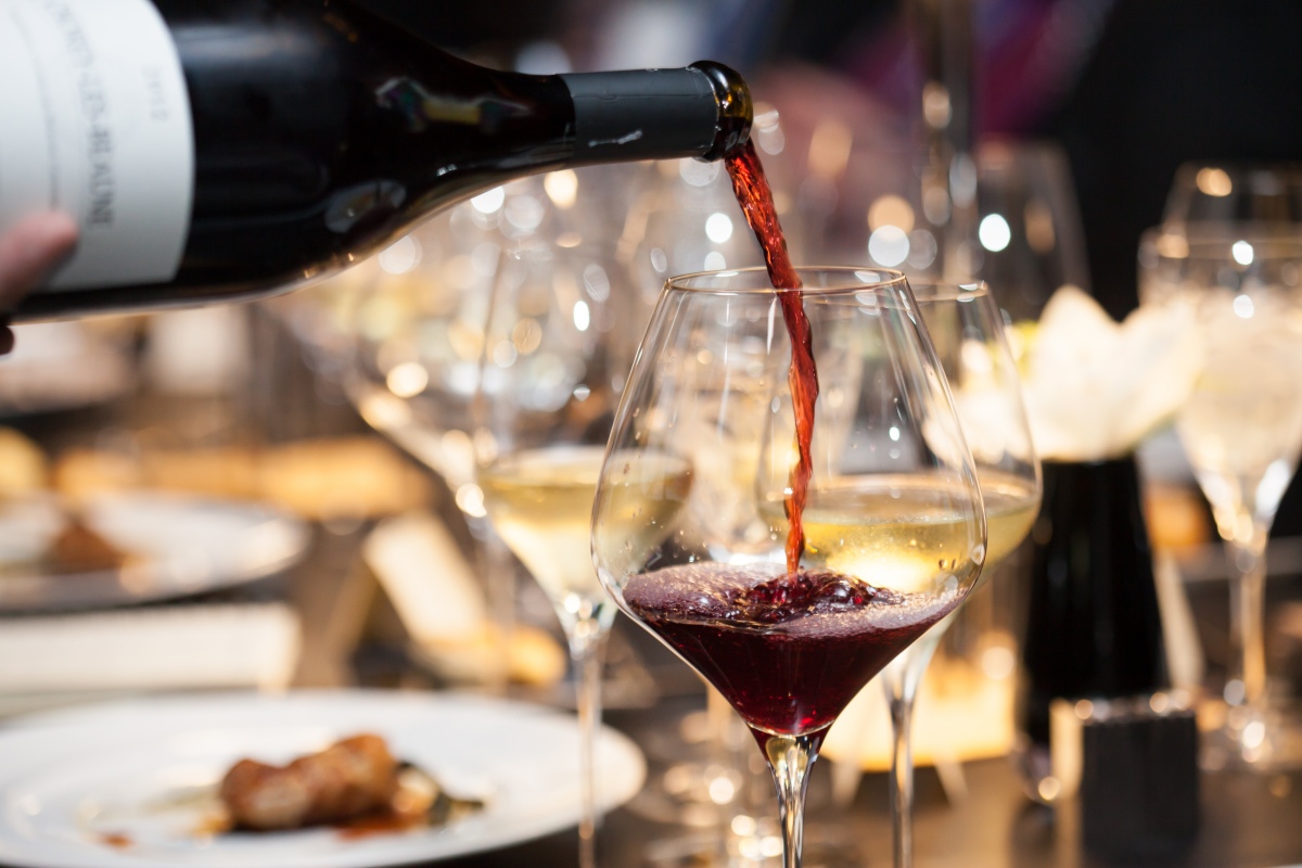waitress pours red wine in a wine glass on the table in restaurant