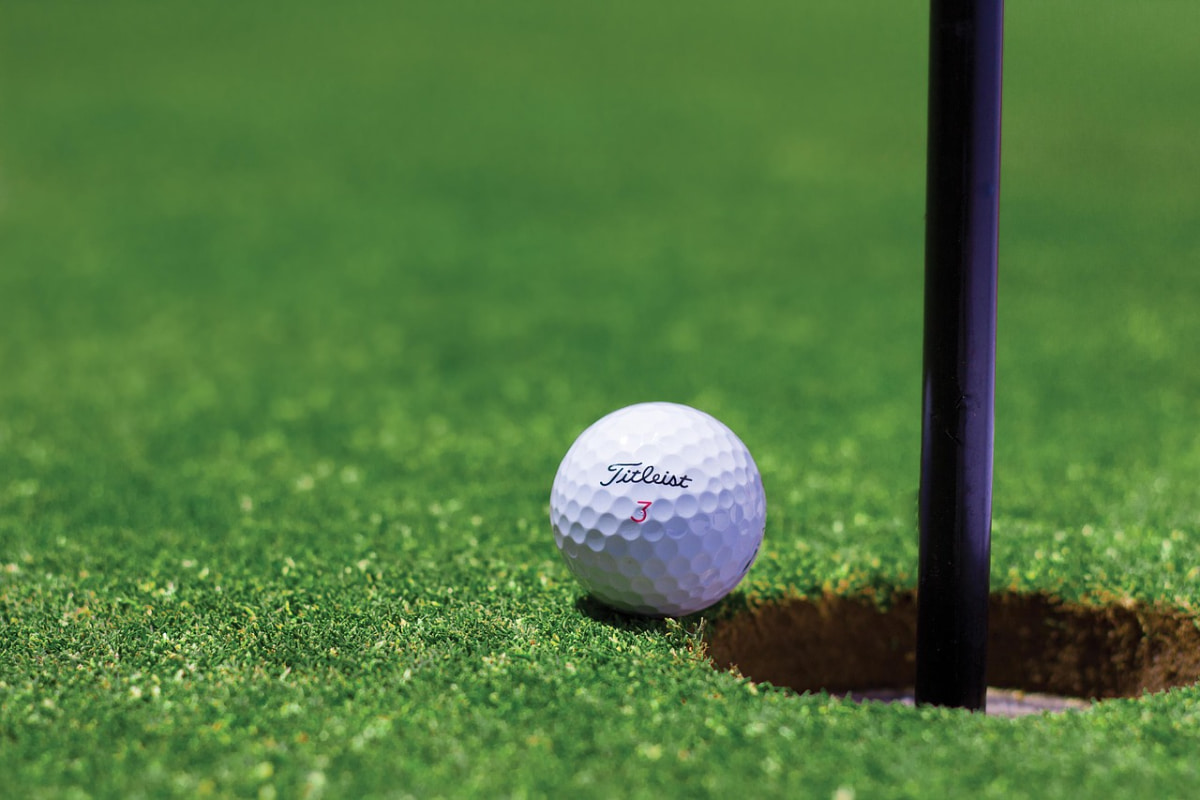 A golf ball teetering on the edge of the hole