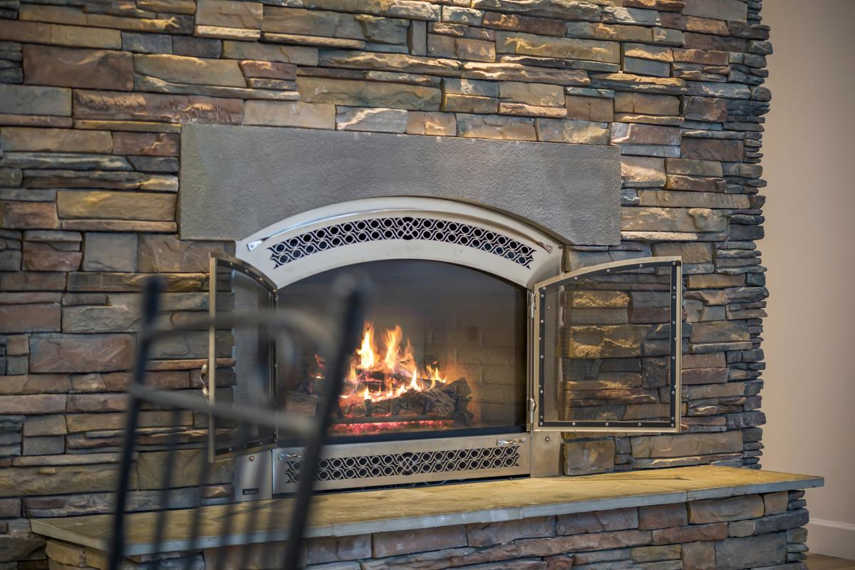 Stone fireplace with flames burning behind open glass doors.