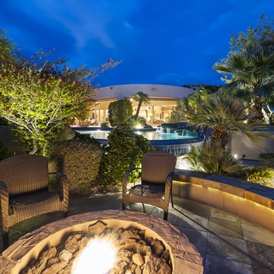 Night view of fire pit seating area with lush landscaping and pool.