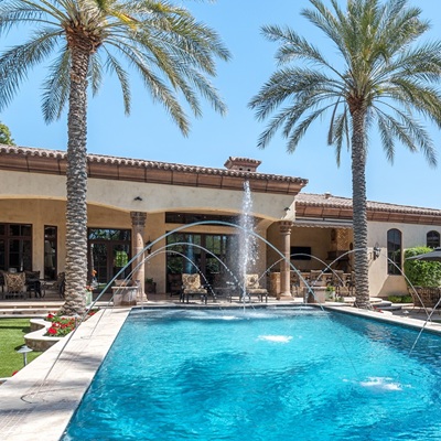 Luxury backyard with pool fountains, palm trees, and patio seating.