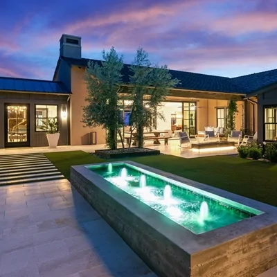 Luxury home patio with green-lit water fountain and outdoor seating at dusk.