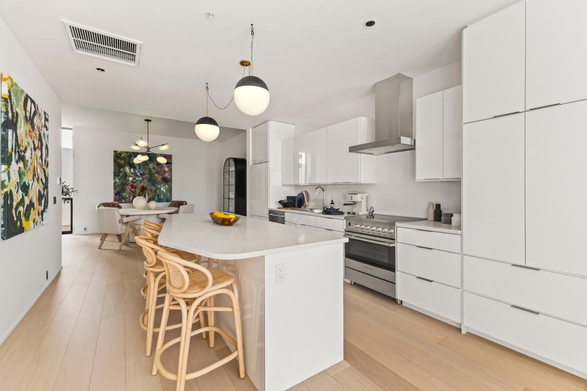 Bright, minimalist kitchen with white cabinetry, a large island, and natural wood accents, opening into a stylish dining space.
