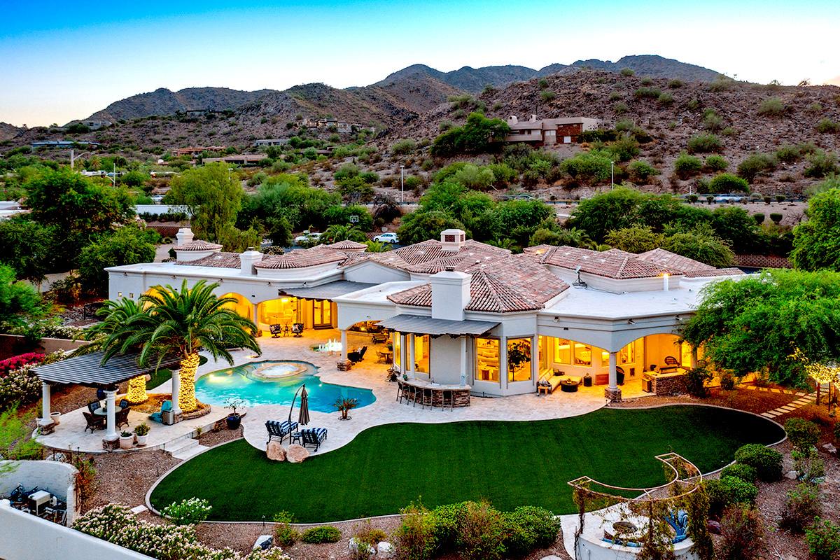 Luxury home in paradise valley with green lawn and pool with a mountain backdrop