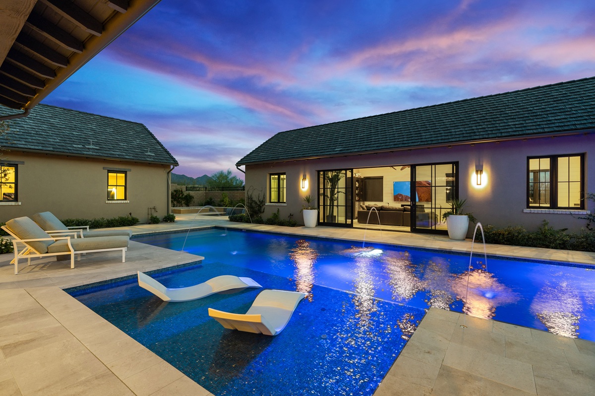 Modern backyard with illuminated pool, lounge chairs, and sunset sky.