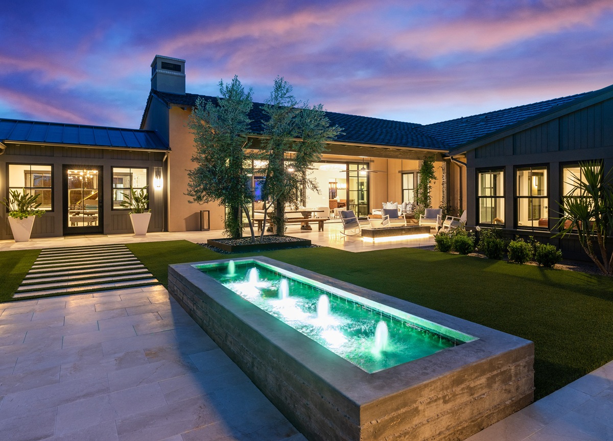 Luxury home patio with green-lit water fountain and outdoor seating at dusk.