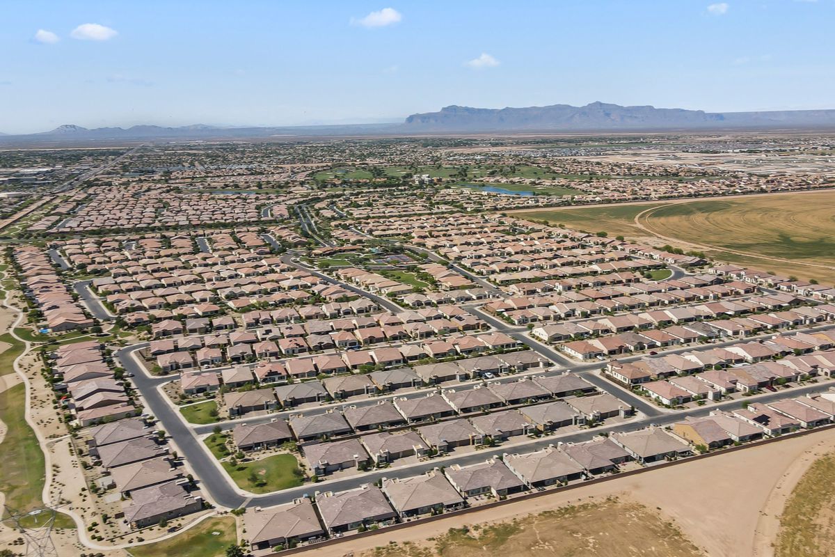 Aerial view of a large suburban neighborhood with rows of similar houses and dry desert landscape in the distance.