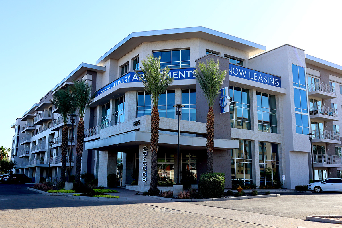 Exterior view of Cascade Luxury Apartments with a “Now Leasing” banner and palm trees in front.