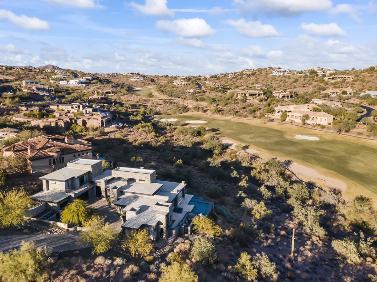 Elevated view of a golf course surrounded by upscale desert homes, with a modern house in the foreground.